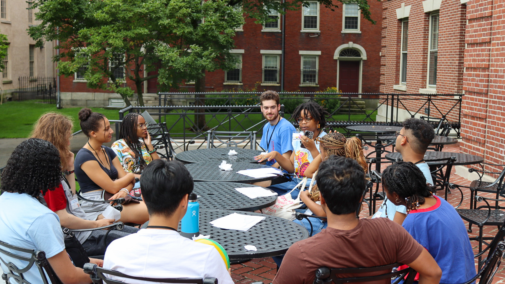A group of diverse students sitting in a circle at outdoor tables on Brown University’s campus, engaged in a lively discussion during the Third World Transition Program